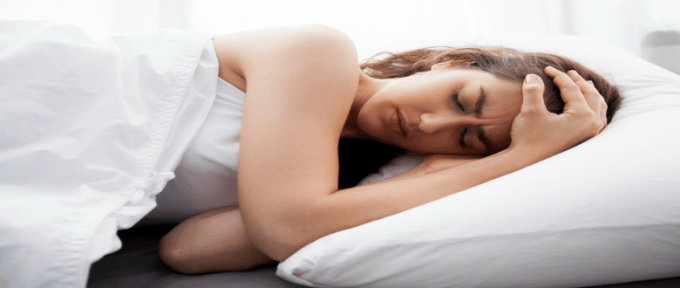 woman lay in bed with headache on white bedding