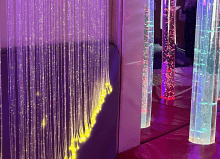 Multisensory room featuring illuminated bubble tubes and hanging fiber optic strands, glowing in calming colors like purple, yellow, and red, designed to provide a soothing environment for sensory stimulation and relaxation.