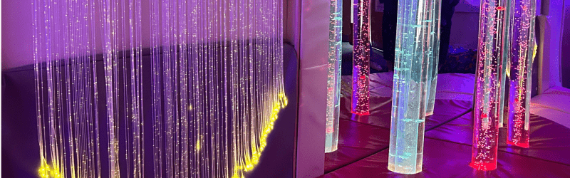 Multisensory room featuring illuminated bubble tubes and hanging fiber optic strands, glowing in calming colors like purple, yellow, and red, designed to provide a soothing environment for sensory stimulation and relaxation.